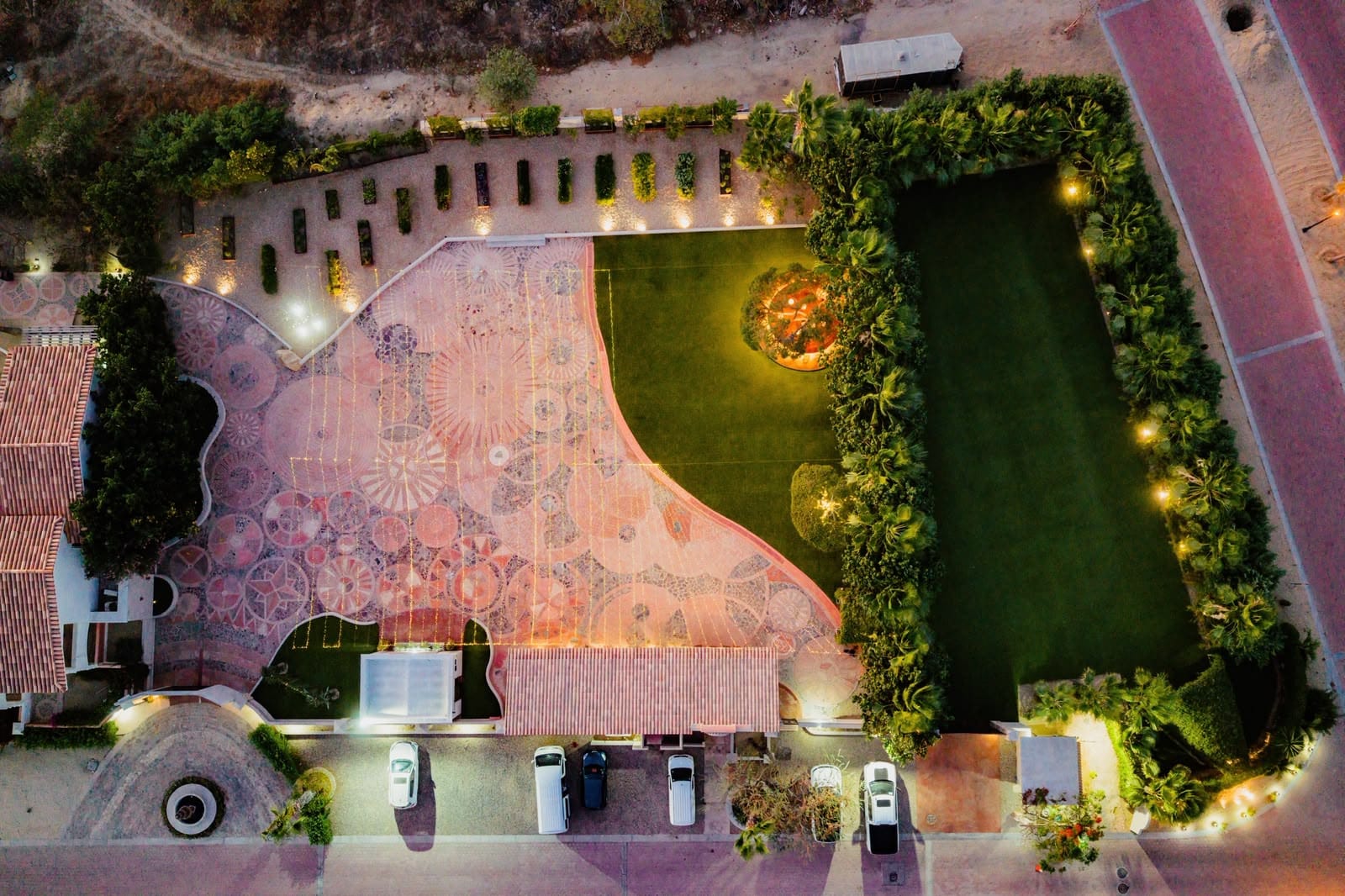 Petunia’s Venue from above at dusk — the hand-laid mosaic terrace, the lawn, and the gardens lit for an evening
